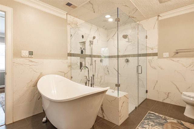 bathroom with a marble finish shower, toilet, crown molding, a freestanding tub, and tile walls