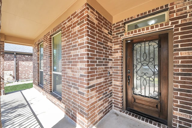 view of exterior entry with a porch and brick siding