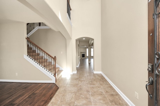 foyer entrance with arched walkways, light tile patterned floors, a towering ceiling, baseboards, and stairway