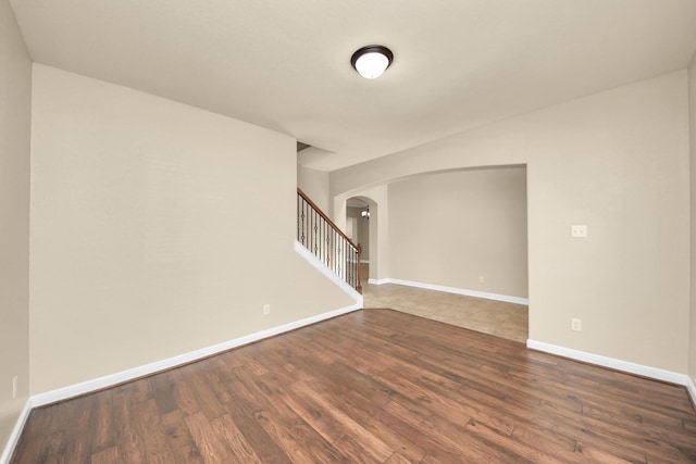 empty room with arched walkways, dark wood-type flooring, stairs, and baseboards