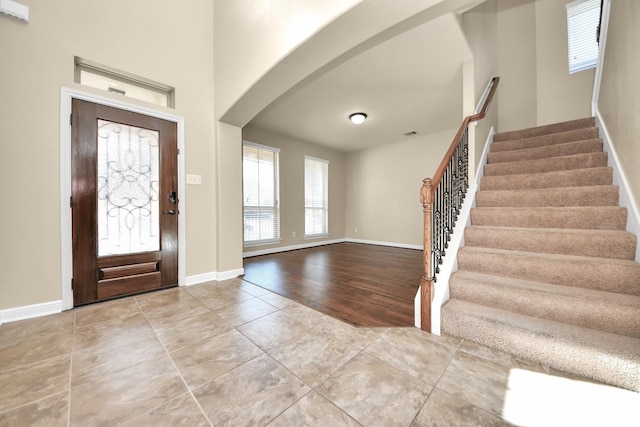 entryway with stairway, tile patterned flooring, arched walkways, and baseboards