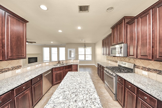 kitchen featuring visible vents, decorative backsplash, appliances with stainless steel finishes, a sink, and light stone countertops