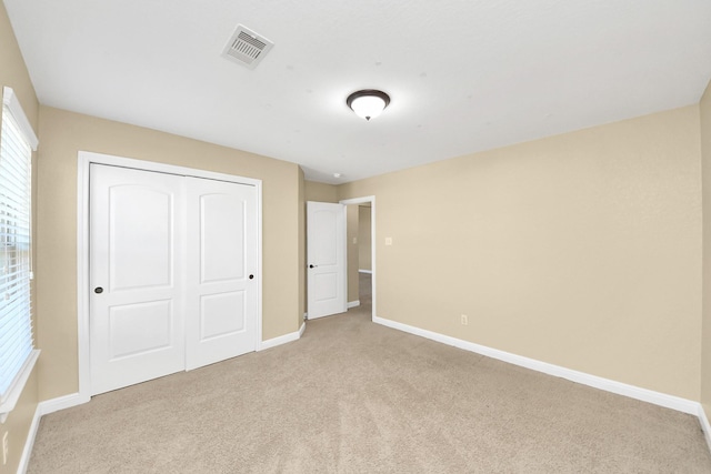 unfurnished bedroom with light colored carpet, a closet, visible vents, and baseboards