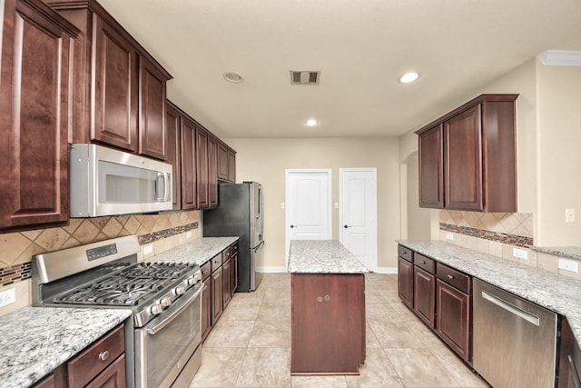 kitchen with visible vents, appliances with stainless steel finishes, a kitchen island, light stone countertops, and baseboards