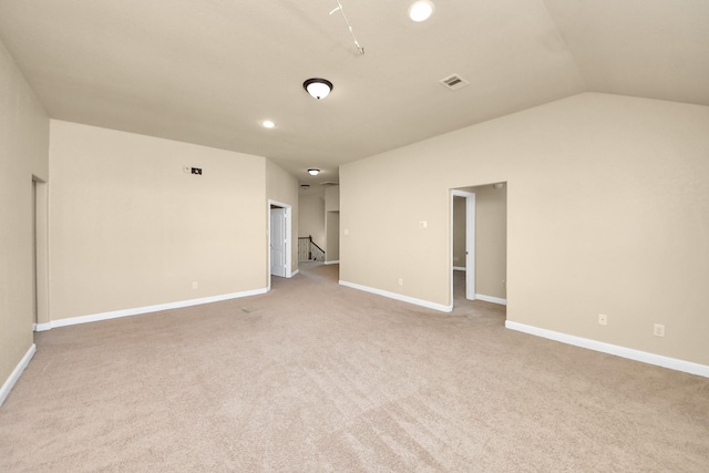 unfurnished room with vaulted ceiling, light colored carpet, visible vents, and baseboards