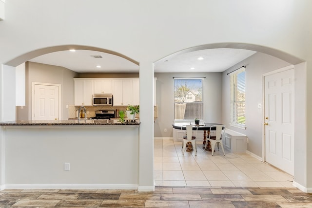 kitchen featuring dark stone countertops, arched walkways, visible vents, and appliances with stainless steel finishes