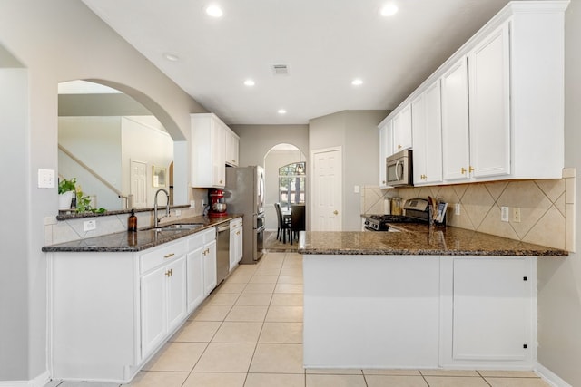 kitchen featuring visible vents, a sink, dark stone countertops, stainless steel appliances, and a peninsula