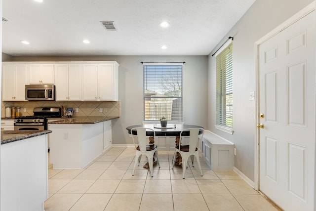 kitchen with light tile patterned floors, visible vents, dark stone counters, stainless steel appliances, and backsplash