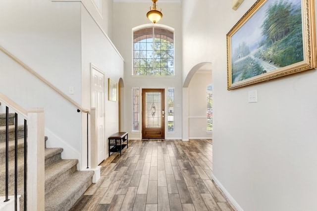 entrance foyer with baseboards, stairway, a high ceiling, wood finished floors, and arched walkways