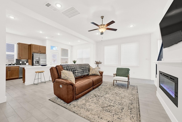 living room featuring recessed lighting, visible vents, a ceiling fan, a glass covered fireplace, and baseboards