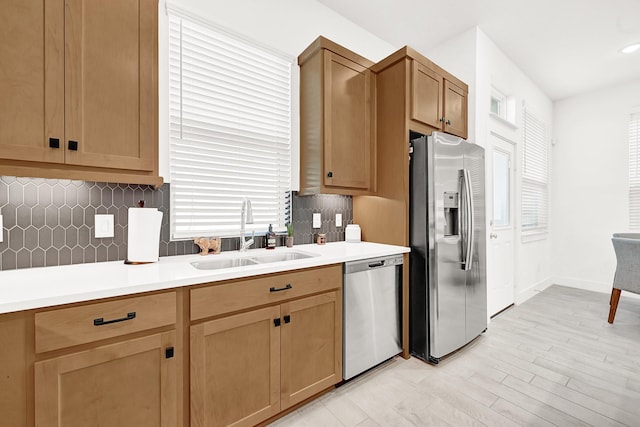 kitchen with light wood finished floors, decorative backsplash, stainless steel appliances, light countertops, and a sink