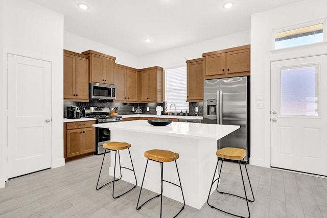 kitchen with tasteful backsplash, light countertops, appliances with stainless steel finishes, a kitchen island, and a kitchen bar