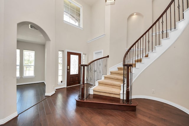 entryway with arched walkways, a high ceiling, wood-type flooring, and baseboards