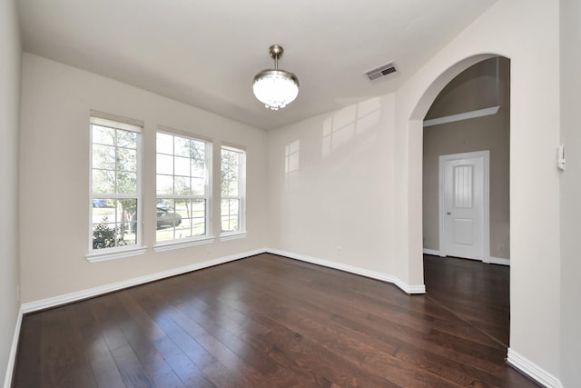 unfurnished room with baseboards, visible vents, arched walkways, and dark wood finished floors