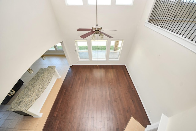 unfurnished living room with a ceiling fan, baseboards, stairway, and a high ceiling