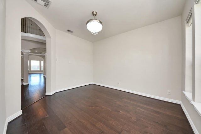 spare room featuring arched walkways, wood-type flooring, decorative columns, and visible vents