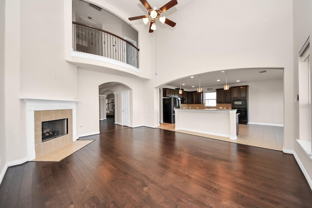 unfurnished living room with arched walkways, wood-type flooring, a ceiling fan, baseboards, and a tiled fireplace