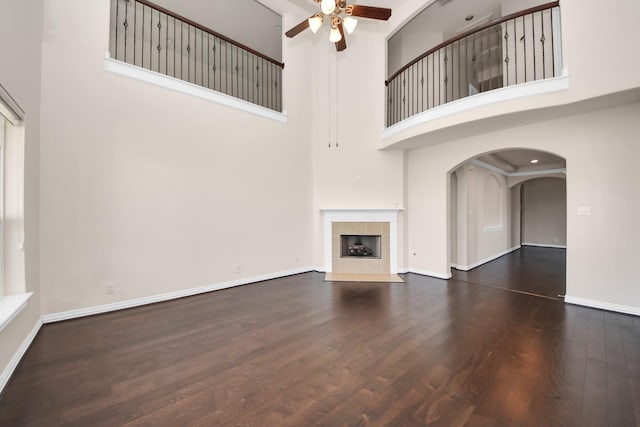 unfurnished living room with a ceiling fan, baseboards, a tiled fireplace, and wood finished floors