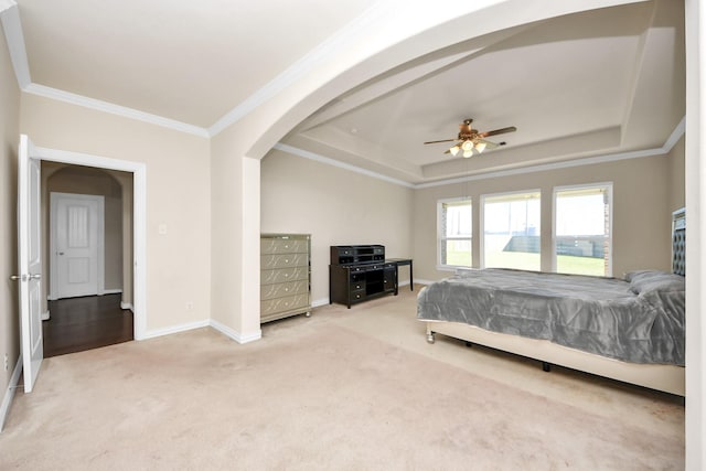 carpeted bedroom with arched walkways, ceiling fan, baseboards, a raised ceiling, and crown molding