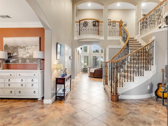 tiled foyer featuring baseboards, arched walkways, a high ceiling, and stairs