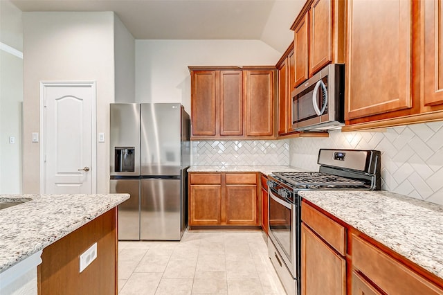 kitchen featuring light tile patterned floors, tasteful backsplash, appliances with stainless steel finishes, brown cabinetry, and light stone countertops