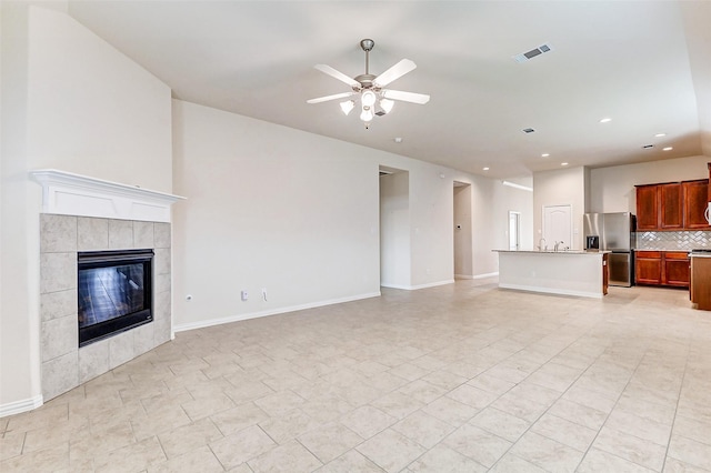 unfurnished living room featuring a tile fireplace, visible vents, ceiling fan, and baseboards