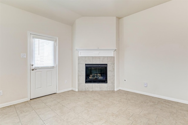 unfurnished living room featuring a tile fireplace, vaulted ceiling, and baseboards