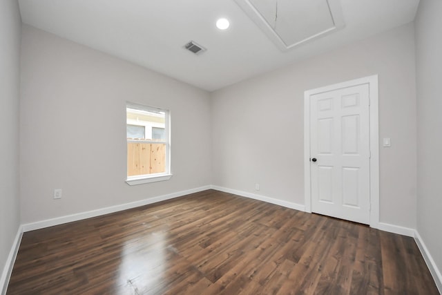 empty room featuring dark wood-type flooring, attic access, visible vents, and baseboards