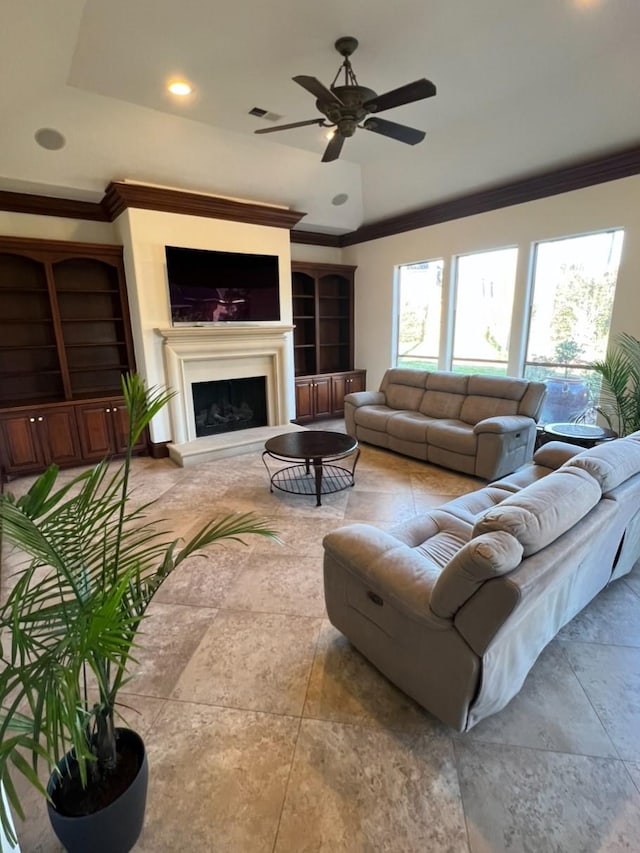 living area with ceiling fan, built in shelves, ornamental molding, and a fireplace with raised hearth