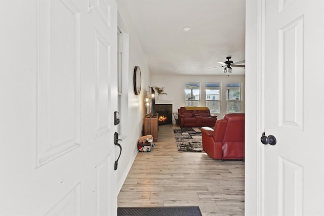 entryway featuring a warm lit fireplace, light wood finished floors, and a ceiling fan