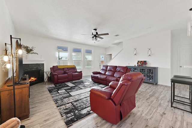 living area featuring a ceiling fan, a warm lit fireplace, a textured ceiling, and light wood finished floors