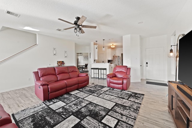 living room featuring a textured ceiling, light wood finished floors, visible vents, and a ceiling fan