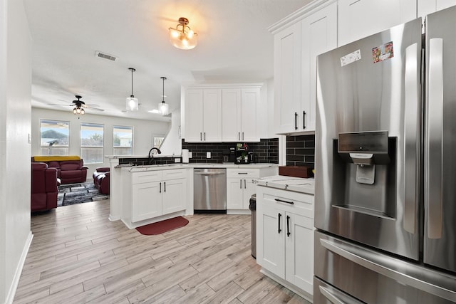 kitchen featuring appliances with stainless steel finishes, open floor plan, a peninsula, light wood-style floors, and backsplash