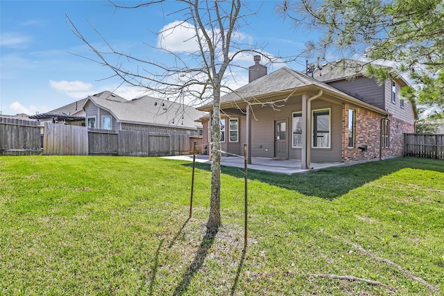 back of house with a patio, a fenced backyard, a chimney, a yard, and brick siding