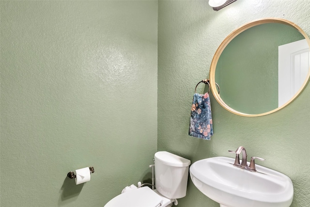 bathroom featuring a textured wall, a sink, and toilet