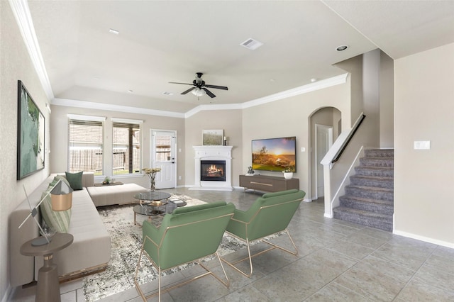 living room featuring crown molding, visible vents, a lit fireplace, baseboards, and stairs