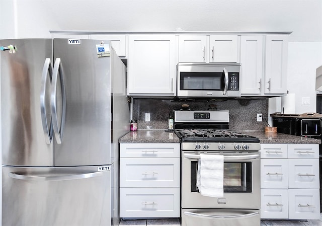 kitchen featuring appliances with stainless steel finishes, dark countertops, white cabinetry, and tasteful backsplash