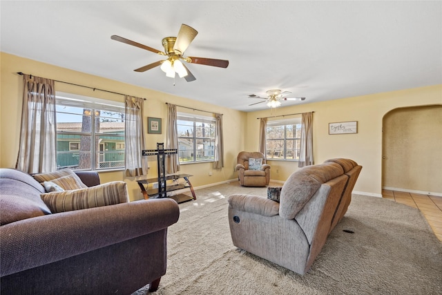 carpeted living room with baseboards, a ceiling fan, and arched walkways