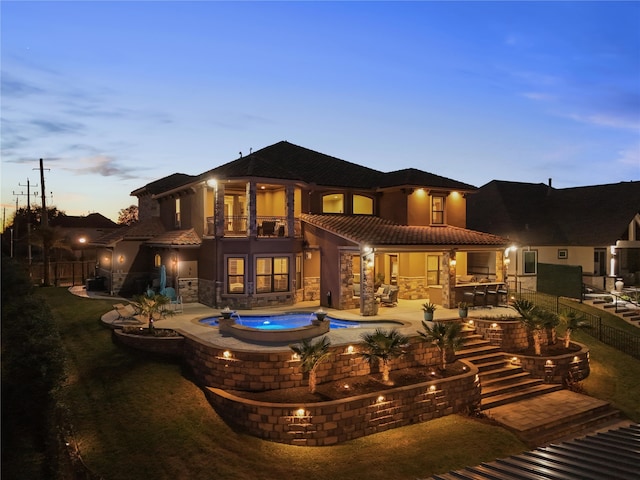 back of house featuring a patio, a balcony, an in ground hot tub, stone siding, and a tiled roof