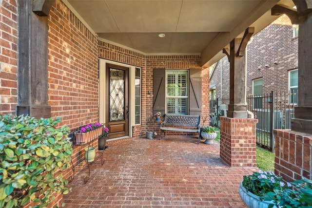 doorway to property with a porch, brick siding, and fence