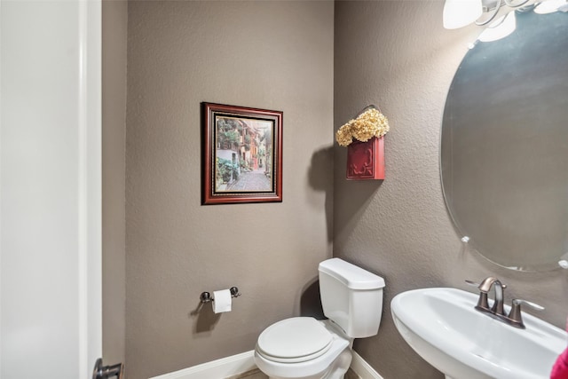 bathroom featuring a textured wall, baseboards, a sink, and toilet