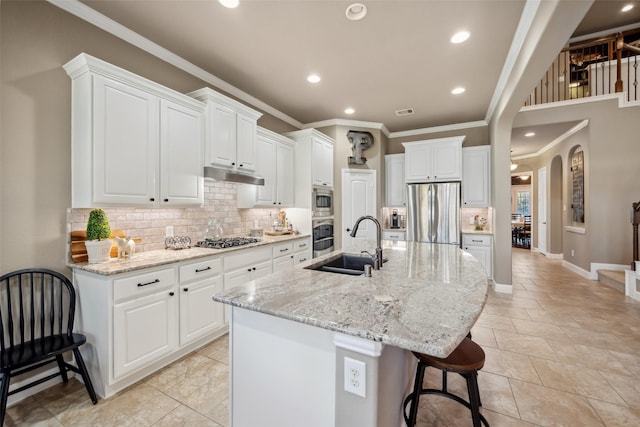 kitchen featuring arched walkways, under cabinet range hood, a breakfast bar, a sink, and appliances with stainless steel finishes