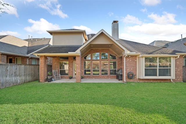 rear view of property with brick siding, a yard, a chimney, a patio, and fence