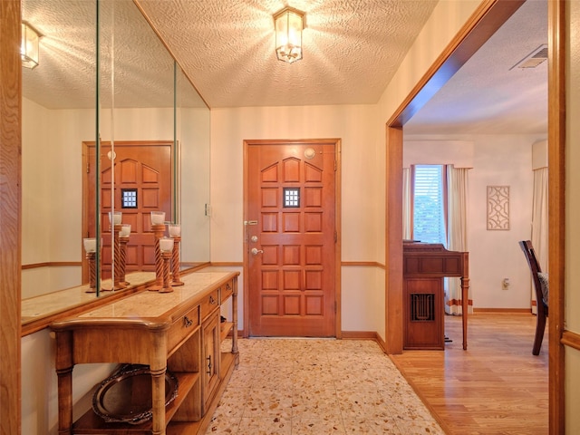 foyer with light wood-type flooring, visible vents, baseboards, and a textured ceiling