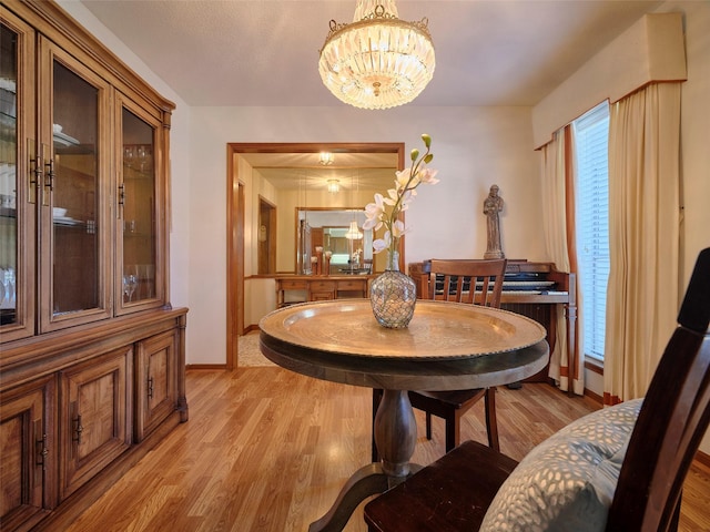 dining area with light wood-type flooring, baseboards, and an inviting chandelier