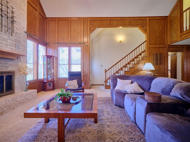 living room with wooden walls, a brick fireplace, stairway, light carpet, and a towering ceiling