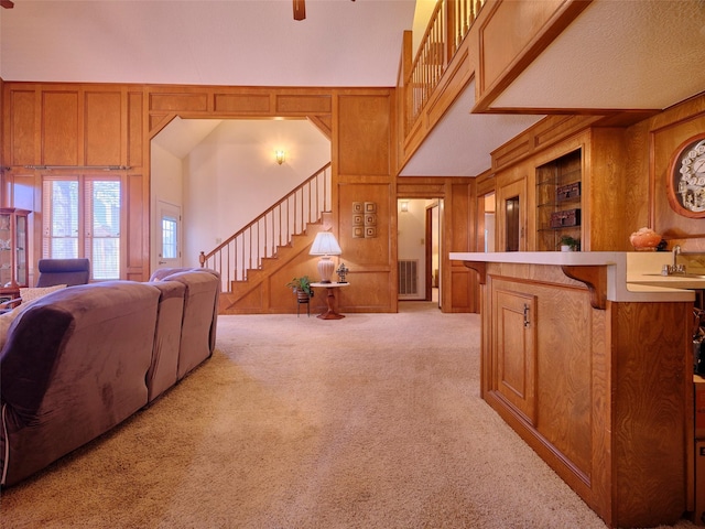 living area featuring ceiling fan, stairway, wood walls, light carpet, and a towering ceiling