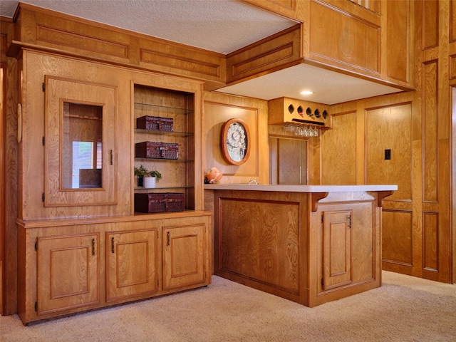 bar featuring light carpet, a bar, wood walls, and a textured ceiling