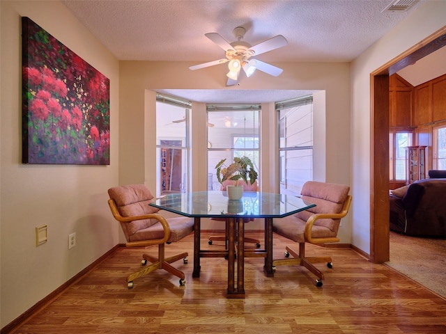 dining area with baseboards, a textured ceiling, light wood-type flooring, and a ceiling fan