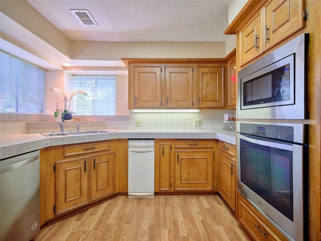 kitchen featuring light wood-style flooring, stainless steel appliances, light countertops, tasteful backsplash, and brown cabinets